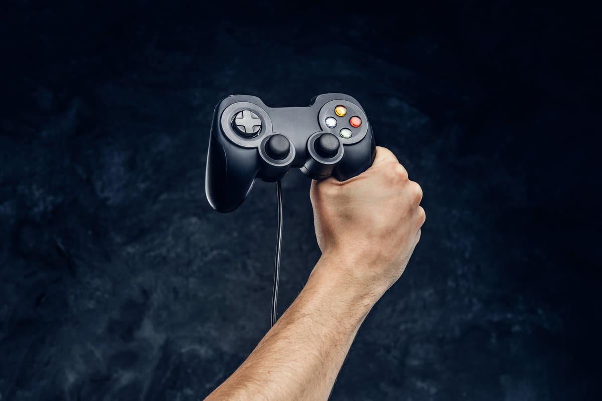 A video game controller held in a gamer's hand against a dark wall