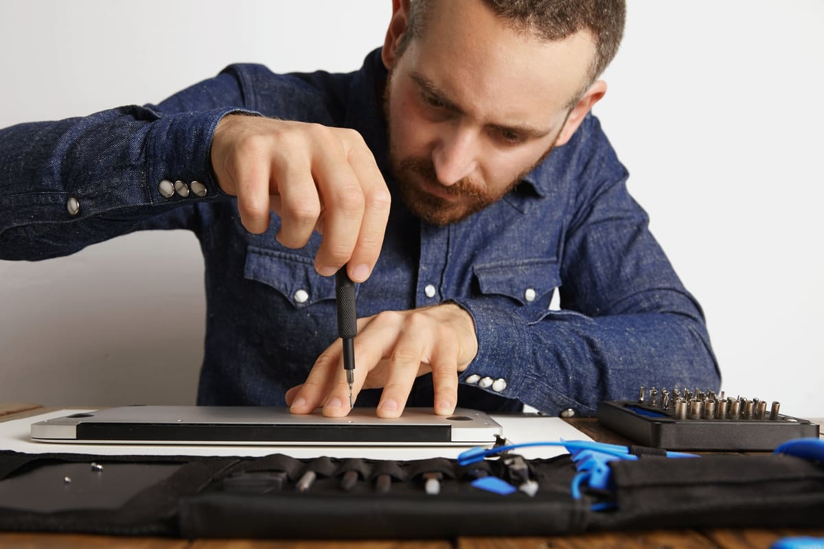 A technician unscrewing the case of a slim metal laptop