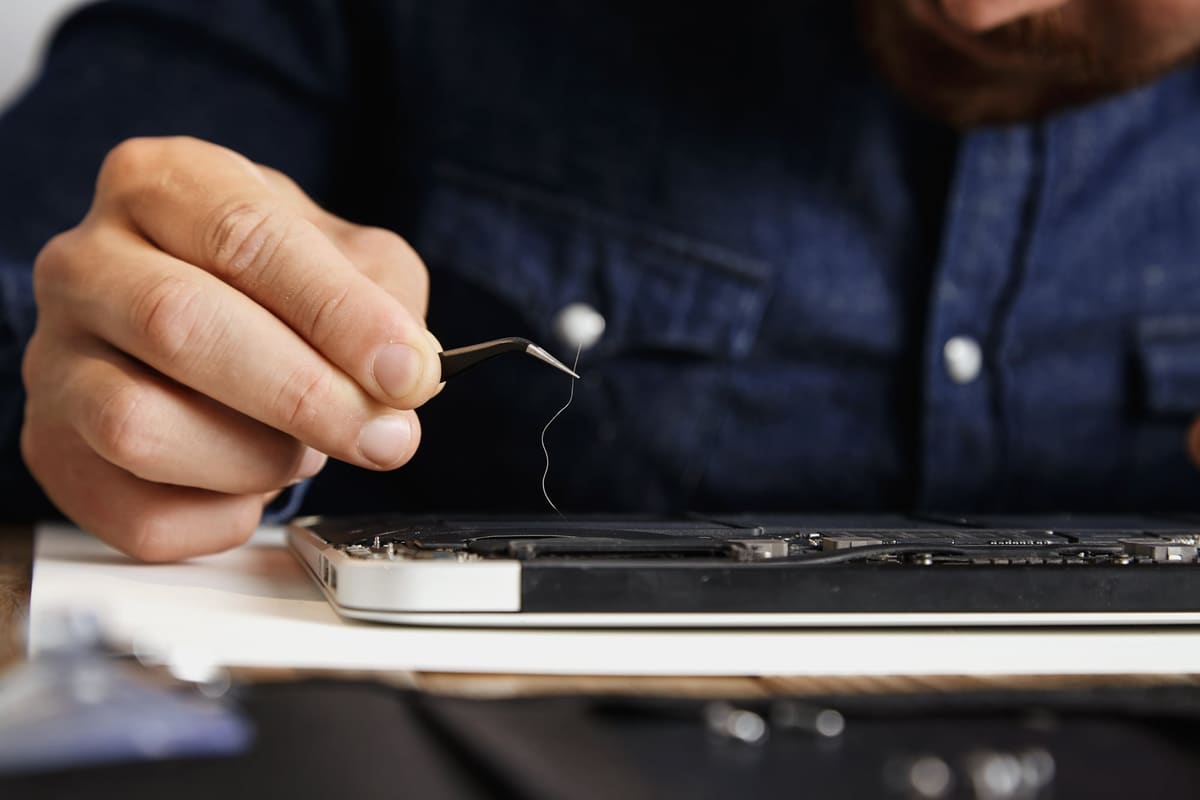 Tweezers removing hair and dust from a laptop cooling fan