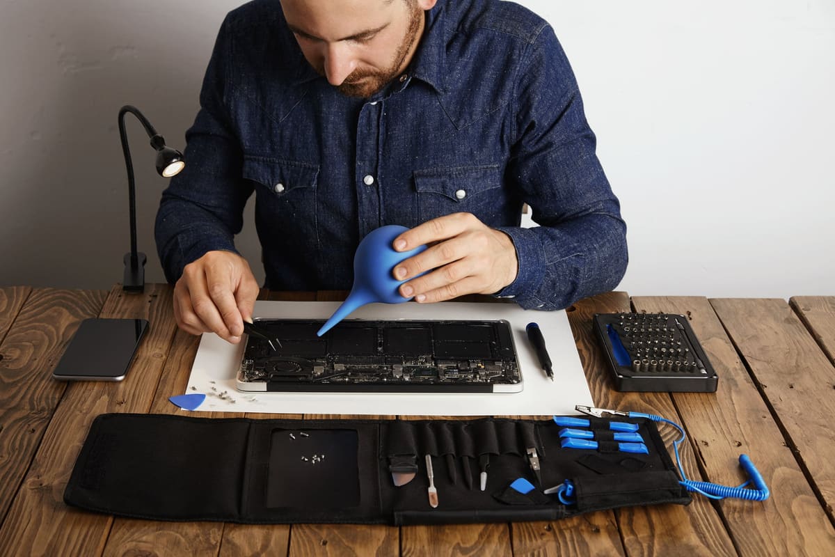 A technician servicing an opened laptop with a toolkit nearby