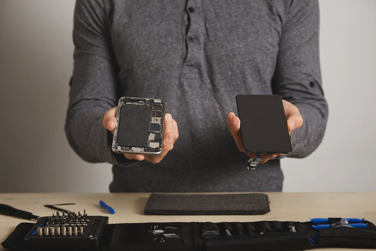 A technician holding a smartphone body and a new replacement screen