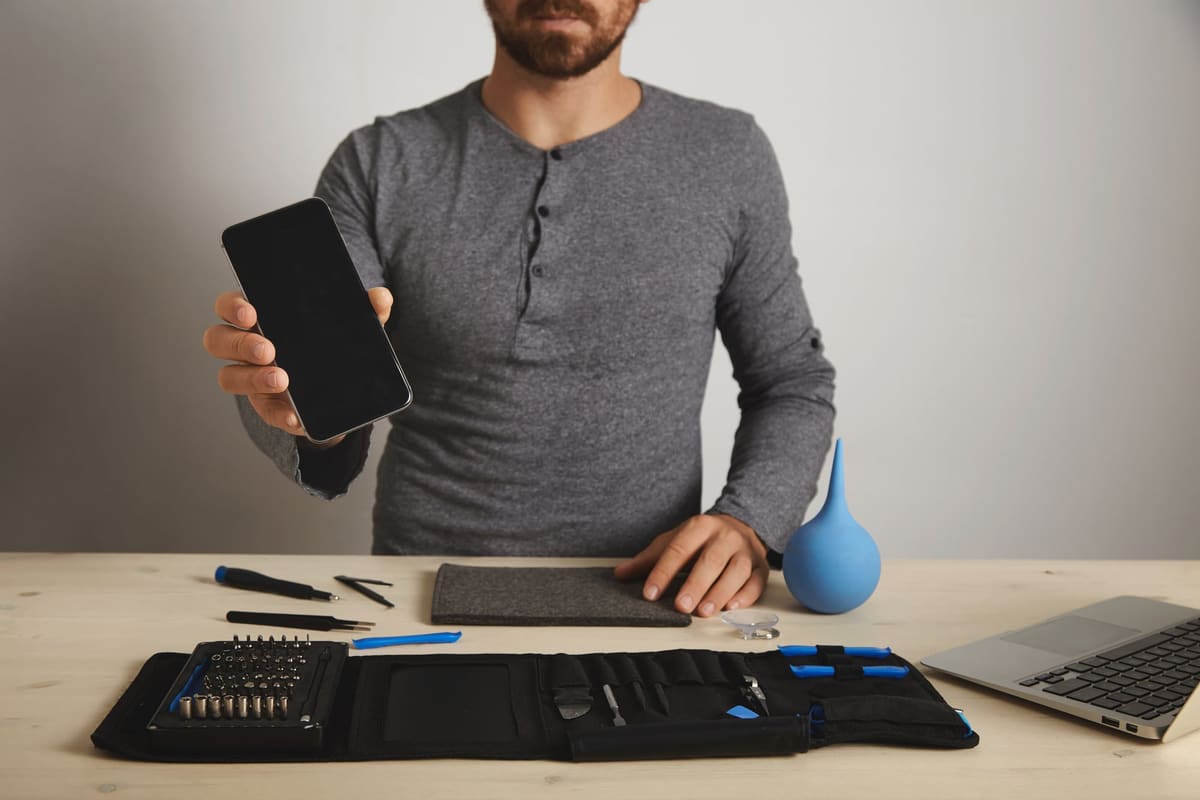 A technician showing a repaired smartphone above his tools
