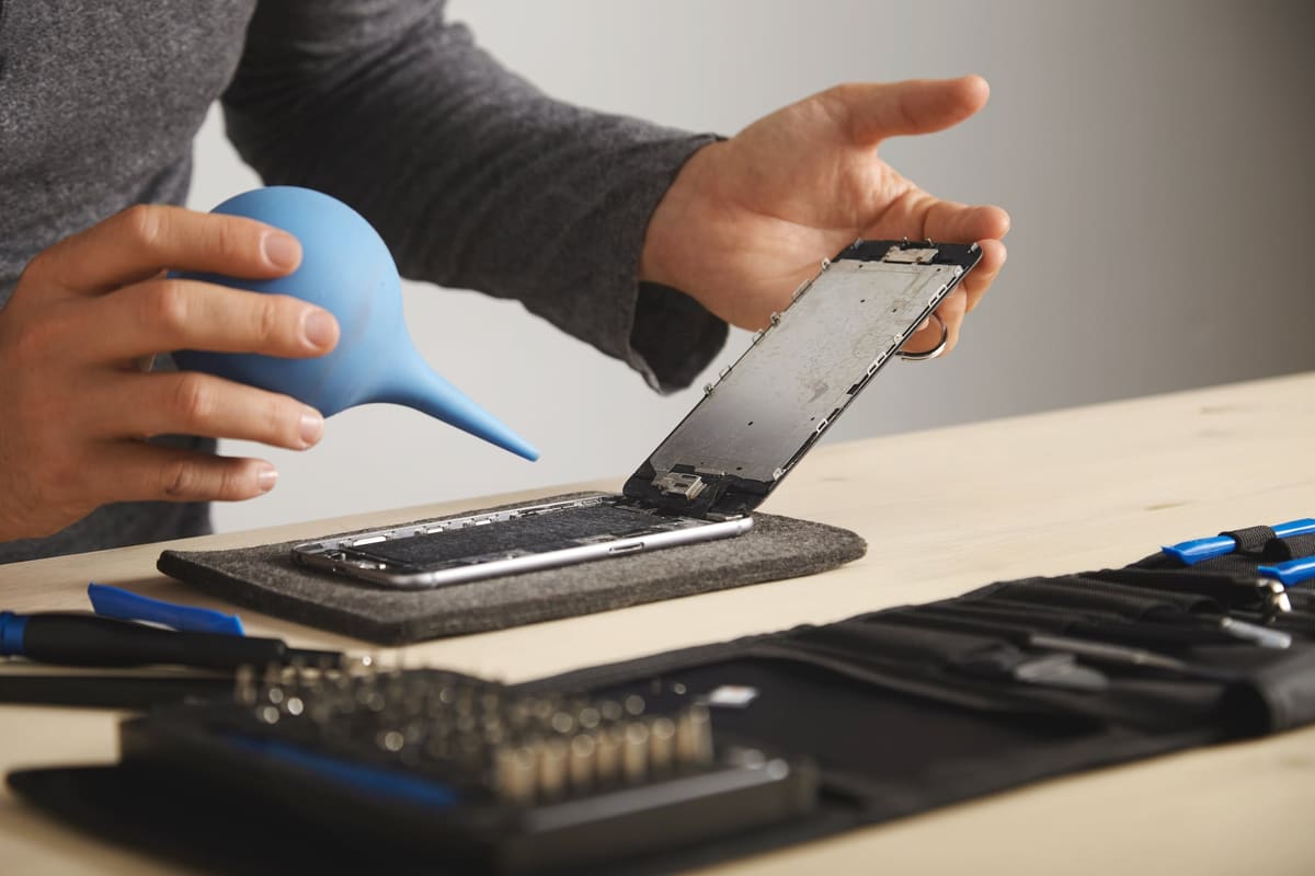A technician carefully blowing dust out of a smartphone