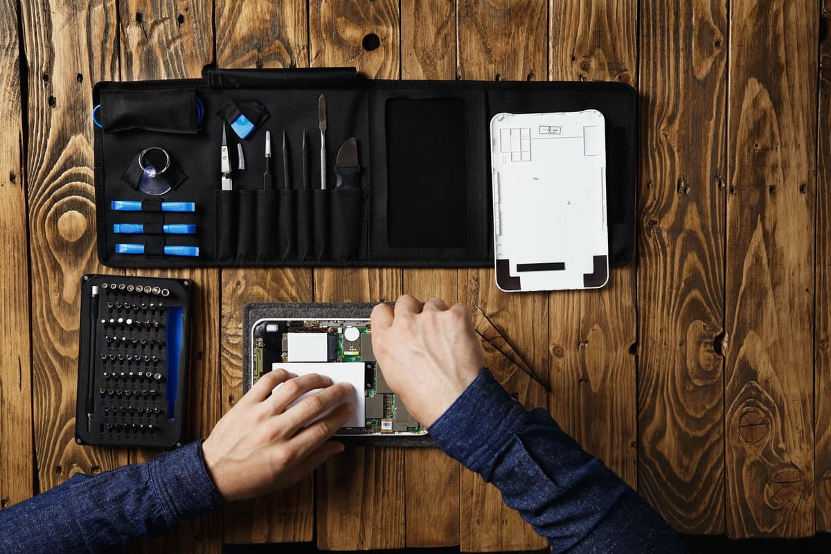A technician working on a broken tablet on a wooden bench